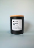 Black candle with a wooden lid labeled 'Moroccan Mint' on a light gray background