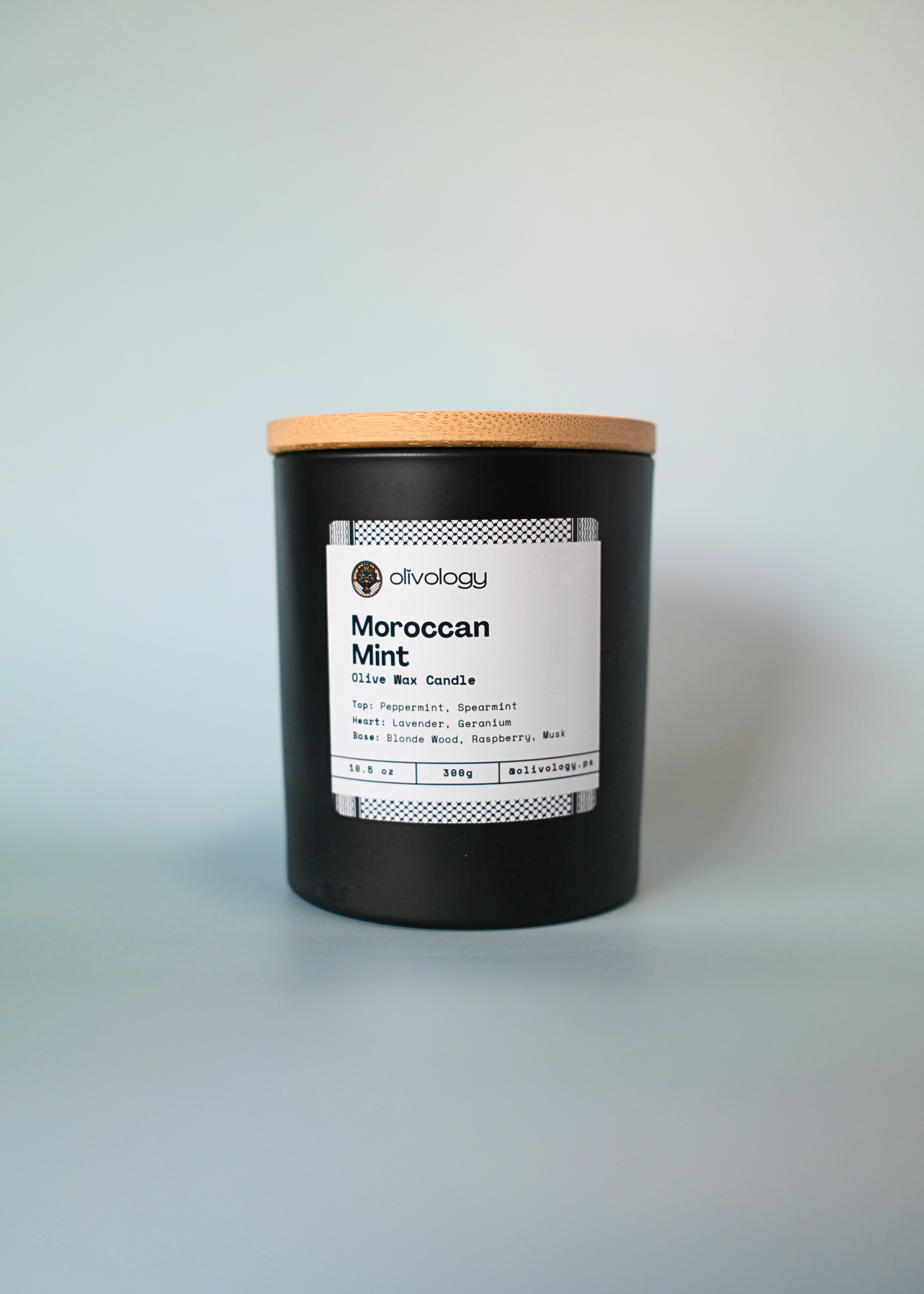 Black candle with a wooden lid labeled 'Moroccan Mint' on a light gray background